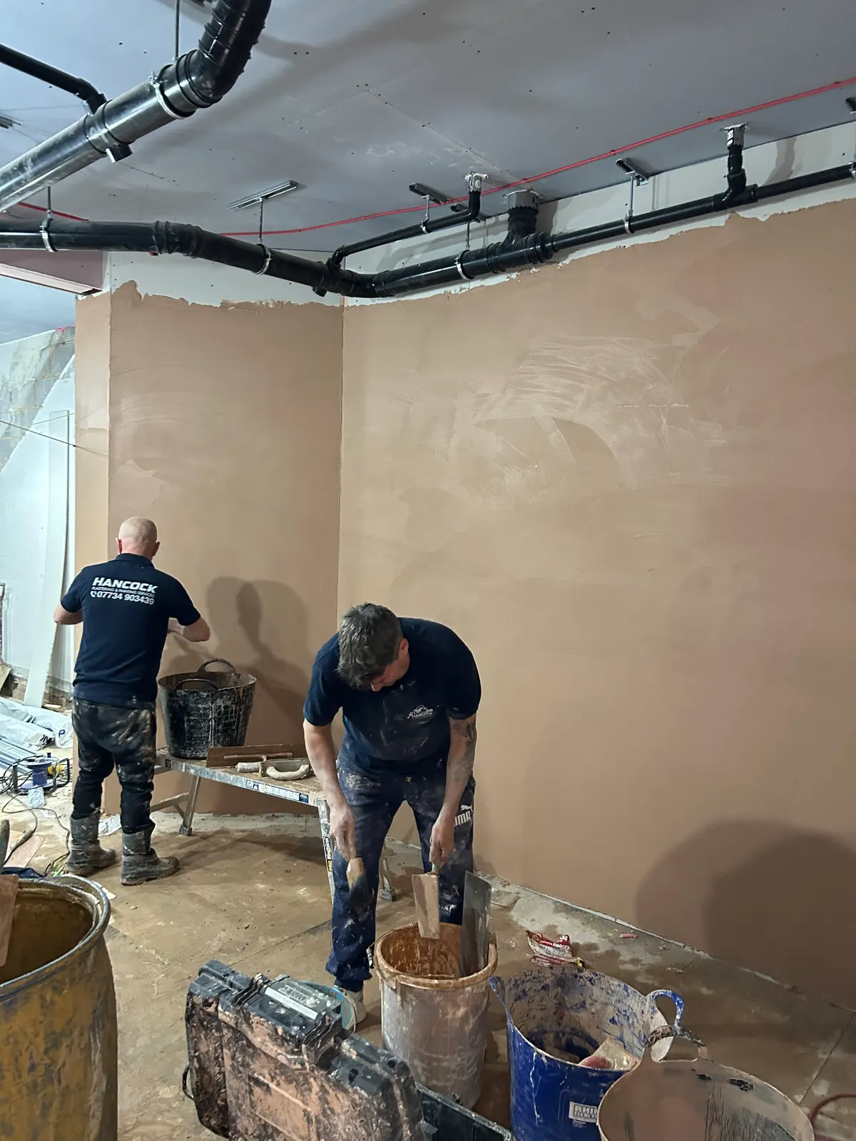 Hancock plasterers skimming a large room with exposed ductwork