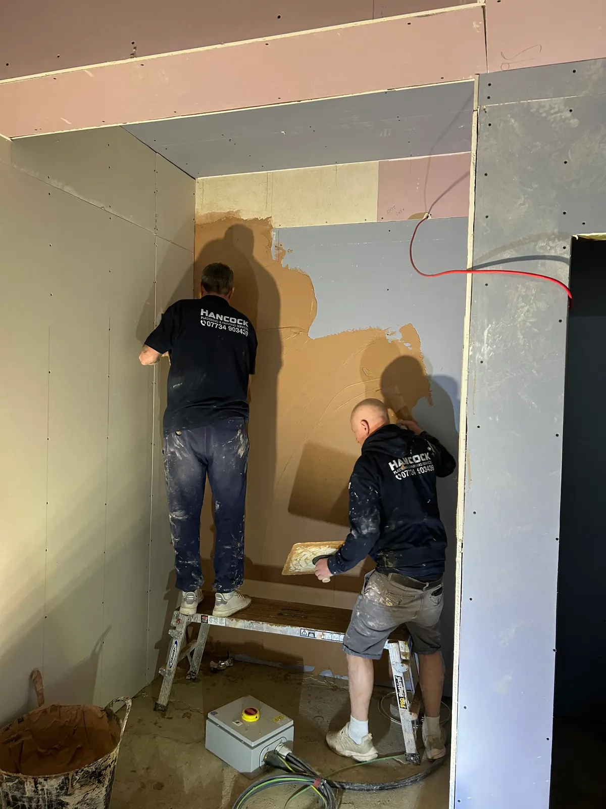 Hancock plastering team skimming walls in a narrow hallway