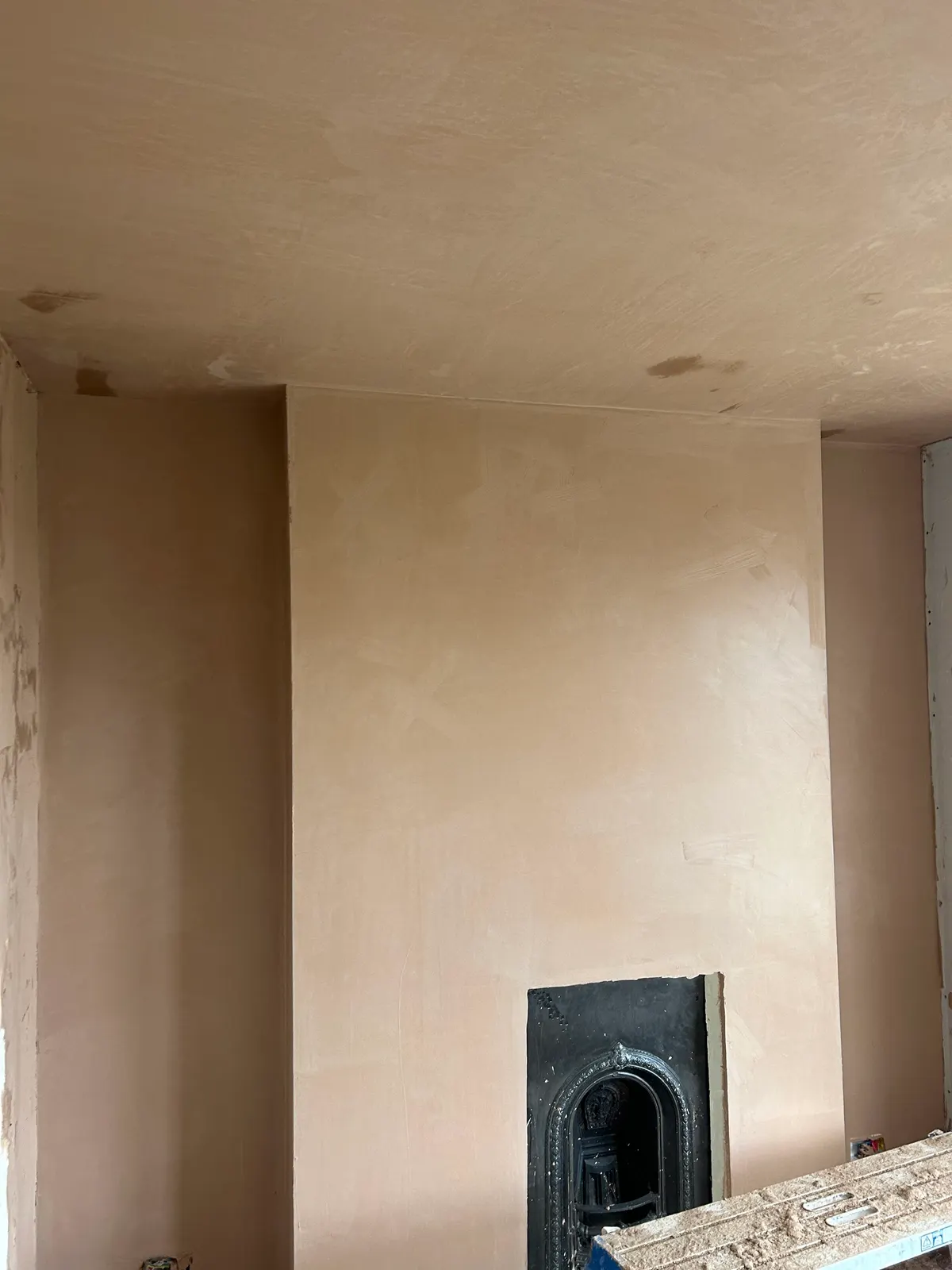 Freshly plastered chimney breast around a cast-iron fireplace with a newly skimmed ceiling