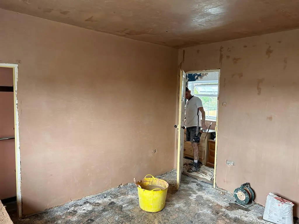 Freshly plastered room with a smooth skim finish and a plasterer working through the doorway